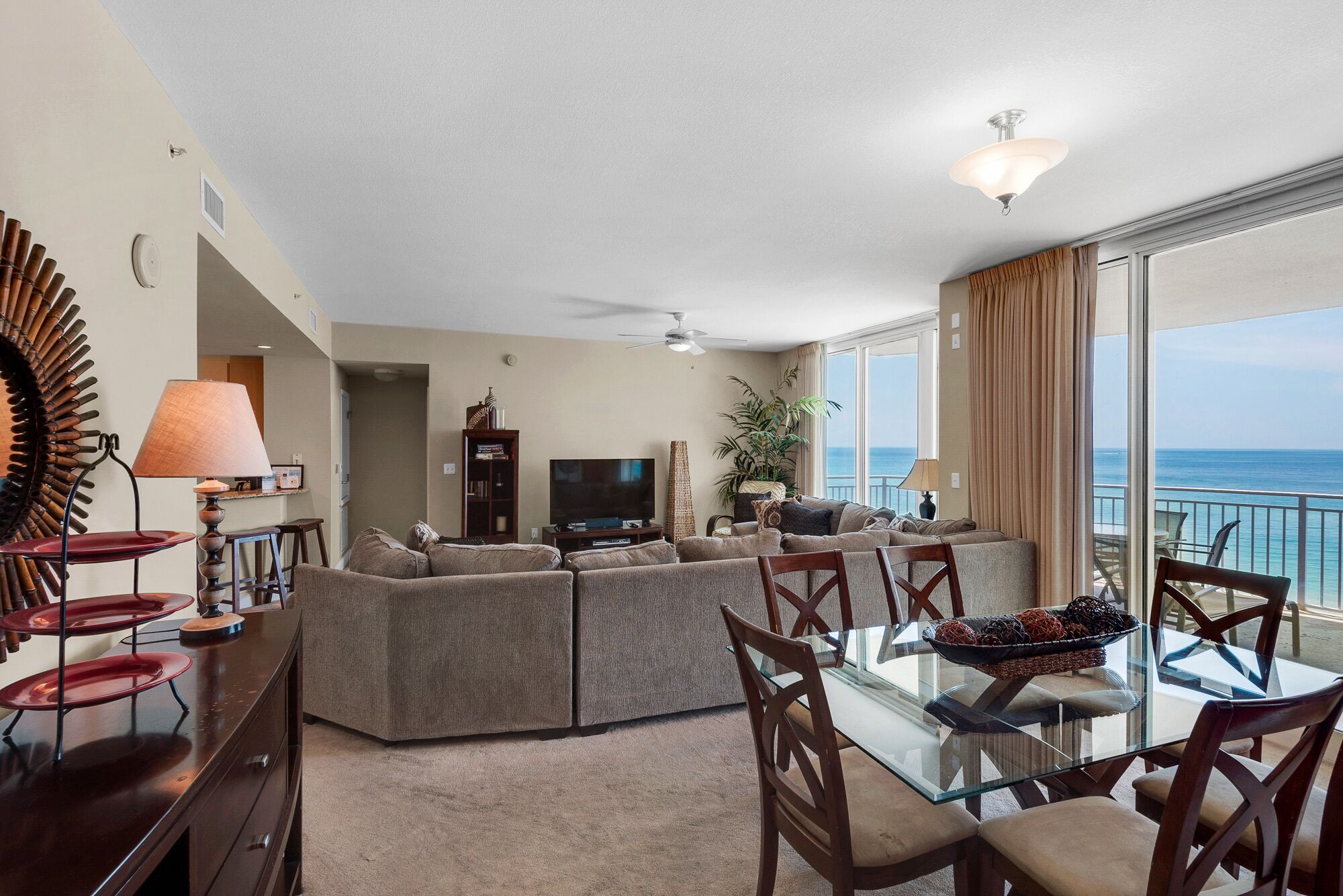 A spacious living room with a large sofa, a glass dining table, and a view of the ocean.