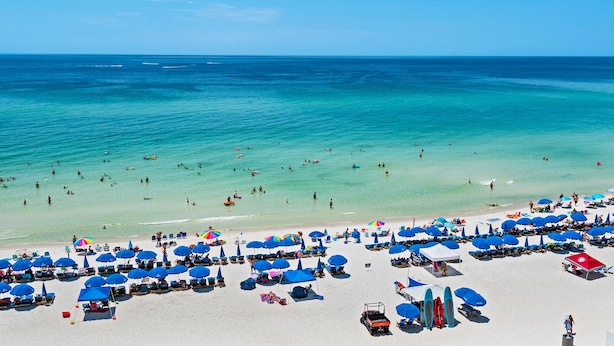 A beach with numerous blue umbrellas and lounge chairs, a sandy shore, and the ocean in the background. - 0602 - Modern Gulf Front Oasis (Panama City Beach)