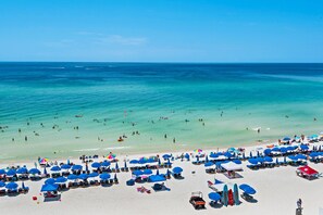 Een strand met vele blauwe parasols en ligstoelen, een zandstrand en de oceaan op de achtergrond.