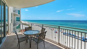 A balcony with a table and chairs overlooking a beach with umbrellas and people. - 0602 - Modern Gulf Front Oasis (Panama City Beach)