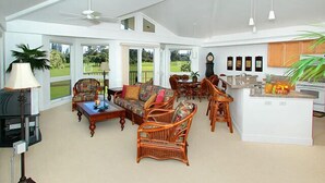 Een ruime woonkamer met een open haard, rieten meubels en uitzicht op een golfbaan.