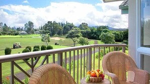Een balkon met rieten meubels en een fruitmand, met uitzicht op een golfbaan.