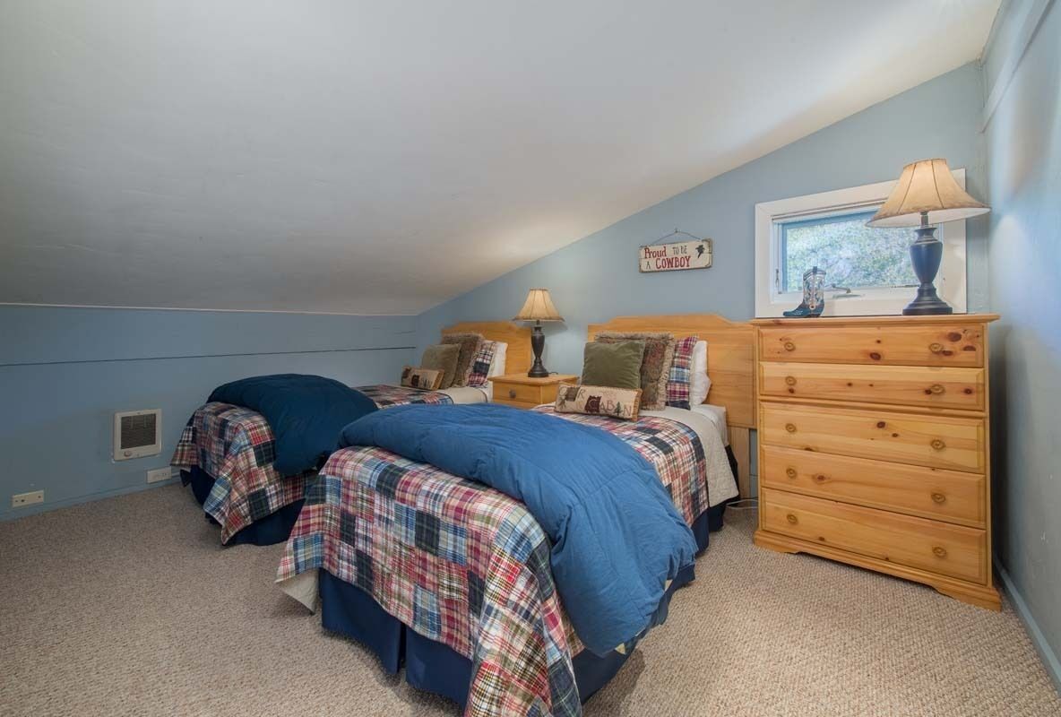A bedroom with two beds, a wooden dresser, a nightstand, and a window with a view.