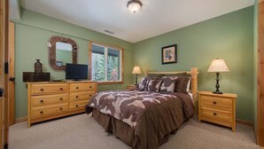Un dormitorio con cama, cómoda, mesitas de noche y ventana con vistas a árboles.