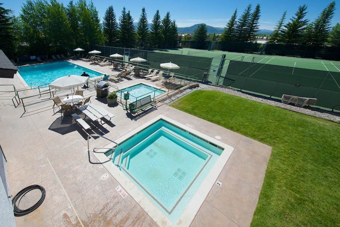A swimming pool area with multiple pools, lounge chairs, umbrellas, and a tennis court.