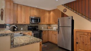 Una cocina con armarios de madera, encimeras de granito, electrodomésticos de acero inoxidable y piso de baldosas.
