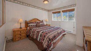 Une chambre à coucher avec un lit, deux tables de chevet avec des lampes, une fenêtre donnant sur des arbres et une commode en bois.