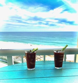 Two glasses of iced drinks on a turquoise table with a view of the beach and ocean.