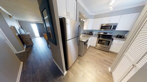 Uma cozinha moderna com eletrodomésticos de aço inoxidável, piso de madeira e armários brancos.