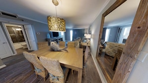 Un coin repas avec une table en bois, des chaises en osier, un luminaire suspendu et un grand miroir.