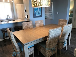 Uma sala de jantar com mesa de madeira e cadeiras de vime, uma cozinha com pia e bancada, e um pendente.