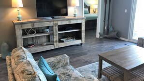 Un salon comprenant un meuble de rangement en bois pour l’équipement audiovisuel, un téléviseur à écran plat, deux lampes, un canapé recouvert d’un tissu à motifs floraux et une table basse.