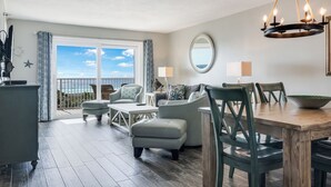 A spacious living area with a balcony overlooking the sea, a dining table with chairs, and a chandelier. - 🌅 Islander #403 – Sunrise Views & Front-Row Beach Action! 🌊🏄‍♂️ (Destin)