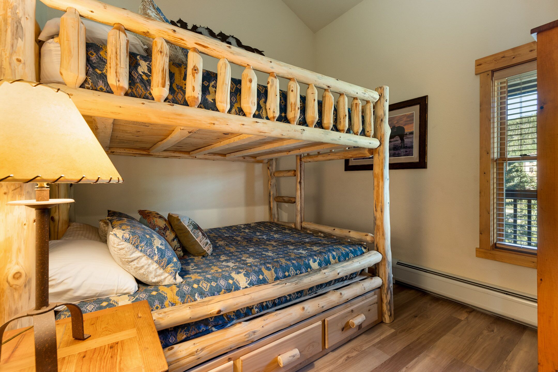 Un lit superposé avec une structure en bois, un matelas à motifs, une lampe de chevet et une fenêtre avec des stores.
