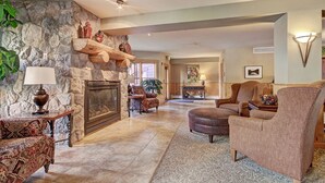 A spacious living room with a stone fireplace, comfortable seating, and a view of the dining area.