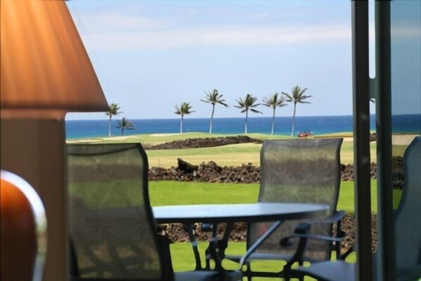 A view from a room with a table and chairs, overlooking a beach with palm trees and a clear sky. - Halii Kai 12H - 3 Bedroom Deluxe Ocean View Hali Kai Vacation Rental (Waikoloa)