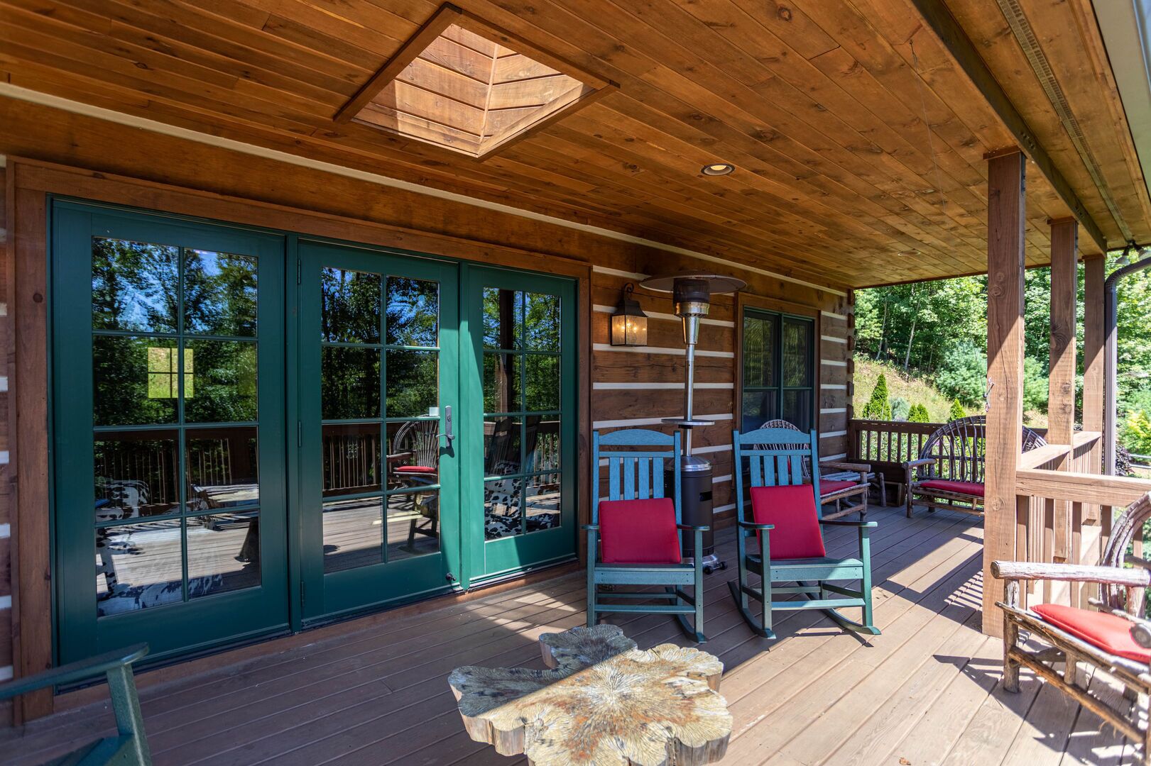 A covered wooden deck with a large sliding glass door, two rocking chairs with red cushions, and a metal heater.