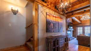 A wooden staircase leading to a loft area with a fireplace, a rustic wooden cabinet, and a large painting of a sunset. - Gratitude - Hot Tub, Pool Table, Covered Decks, 5 minutes to Boone (Blowing Rock)
