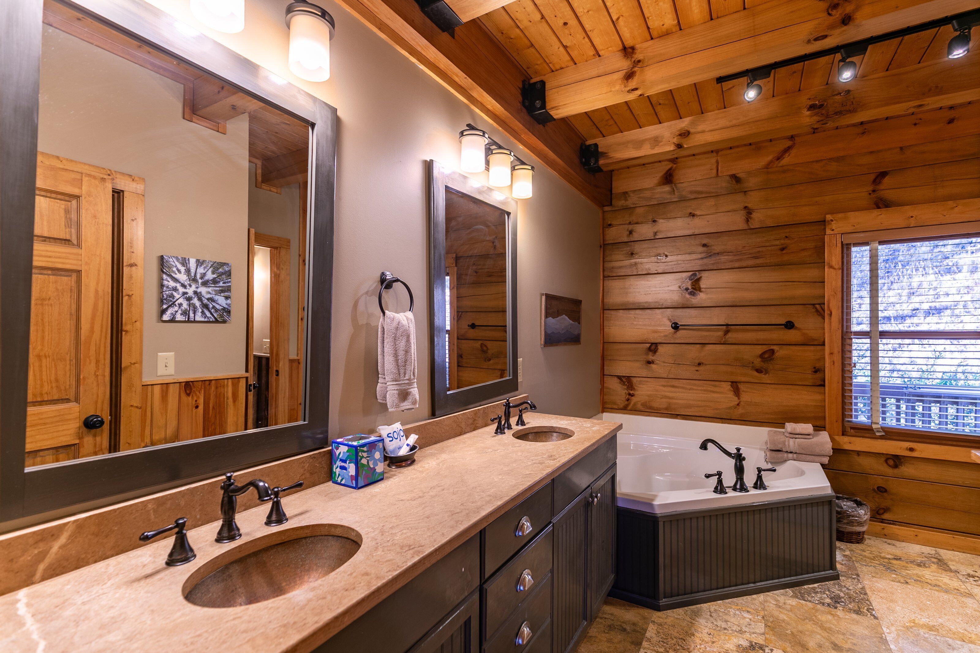A wooden cabin bathroom with two sinks, a large mirror, and a bathtub.