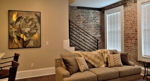 A living room with a brick wall, a staircase, a sofa with cushions, and a painting on the wall. - 1890-1930 Historic Politics Themed condo, 2 blocks from French Quarter (New Orleans)