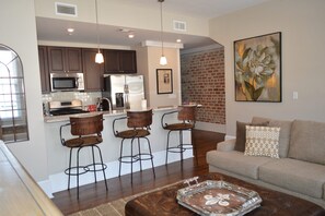 Una cocina moderna con electrodomésticos de acero inoxidable, una pared de ladrillo y una zona de comedor con taburetes de bar.