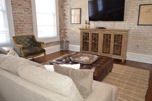 Un salon avec un mur en briques, un téléviseur fixé au-dessus d’un meuble en bois et un canapé en cuir.