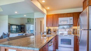 A modern kitchen with granite countertops, stainless steel appliances, wooden cabinets, and a large island with a sink. - Pali Ke Kua 245 .. Updated Oceanfront Condo, Views are Expansive! (Princeville)