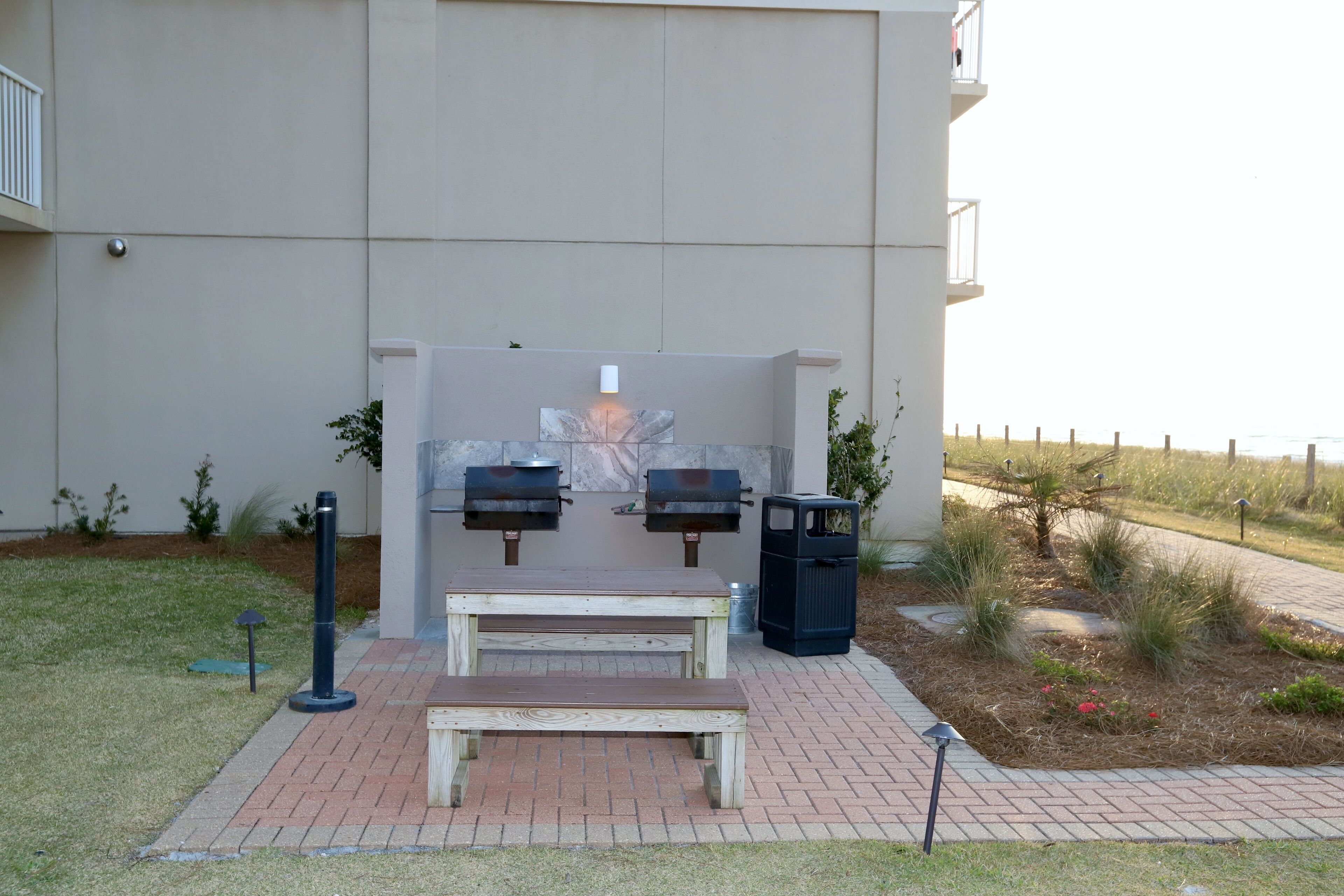 An outdoor seating area with a table and benches, a barbecue grill, and a trash can.