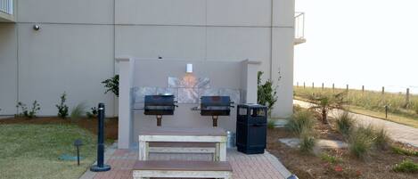 An outdoor seating area with a table and benches, a barbecue grill, and a trash can.