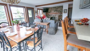 A dining area with a wooden table and chairs, a stone fireplace, and a view of the outdoors. - JHRL - Rendezvous B4, Comfortable Slope-side Condo, Hot tub next door (Teton Village)