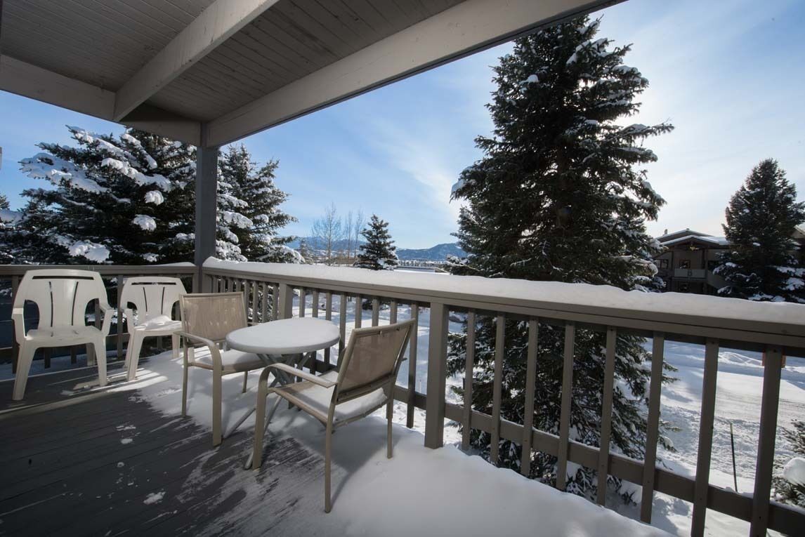 A covered outdoor area with a table and chairs, surrounded by snow-covered trees and a view of a snowy landscape.