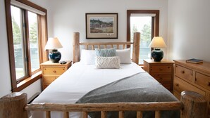 A bedroom with a wooden bed, two bedside tables, a nightstand, a framed picture on the wall, and large windows. - JHRL - Rendezvous B4, Comfortable Slope-side Condo, Hot tub next door (Teton Village)
