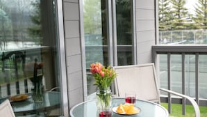 A glass table with chairs on a wooden deck, a vase with flowers, and a glass of red wine. - JHRL - Rendezvous B4, Comfortable Slope-side Condo, Hot tub next door (Teton Village)