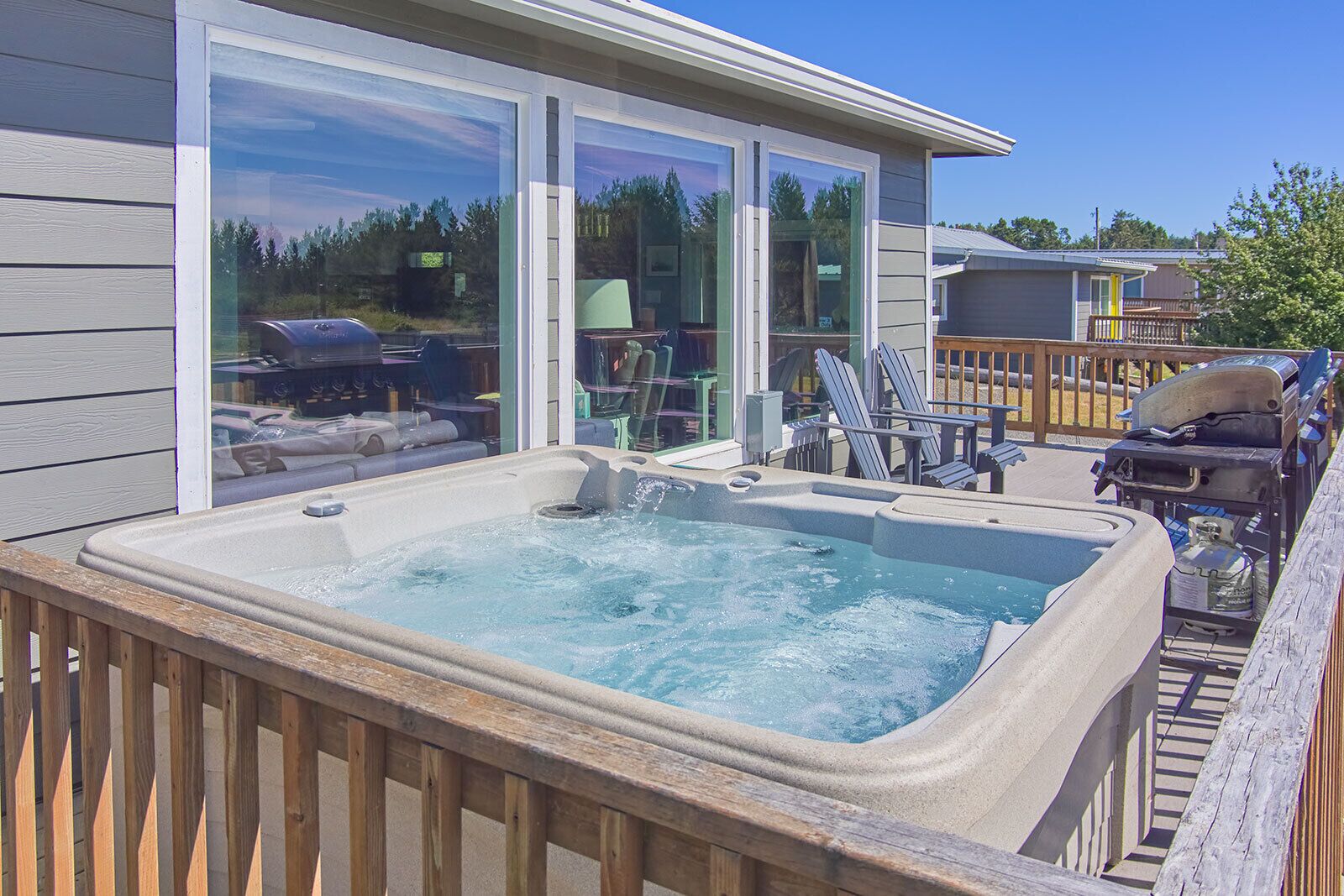 A hot tub in a wooden deck area with a view of a house and outdoor furniture.
