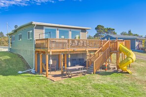 A two-story house with a wooden deck, a slide, and a covered patio area.