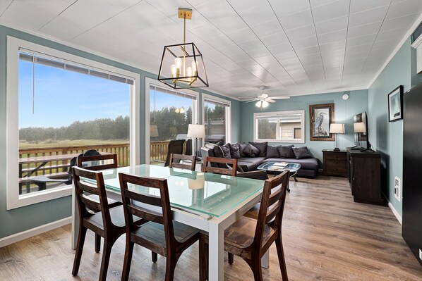 A dining area with a glass-top table and wooden chairs, a ceiling fan, and a view of the outdoors.