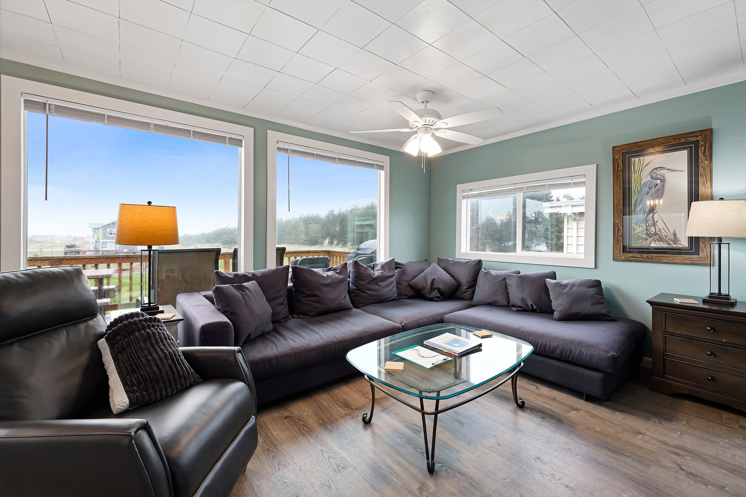 A modern living room with a sectional sofa, a glass coffee table, and a ceiling fan.