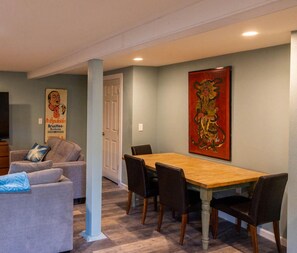 A dining area with a wooden table and chairs, a grey sofa with a blue throw pillow, and a large red artwork on the wall.