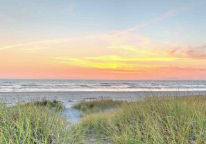 A beach with grass in the foreground and a sunset in the background.