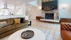 A modern living room with a stone fireplace, a sofa, a coffee table, and a TV mounted above the fireplace. - JHRL - Wind River #2, Well-Appointed and Well-Located - 1 minute from Ski Access (Teton Village)