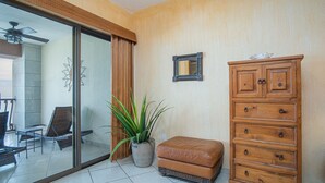 Een kamer met een schuifdeur naar een balkon, een houten dressoir, een potplant en een klein pouf.
