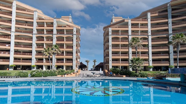 Een hotel met meerdere verdiepingen, een centraal gelegen zwembad en palmbomen.