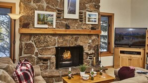 A cozy living room with a stone fireplace, a flat-screen TV, and a comfortable couch. - JHRL - Rendezvous D4, Great location for families (Teton Village)