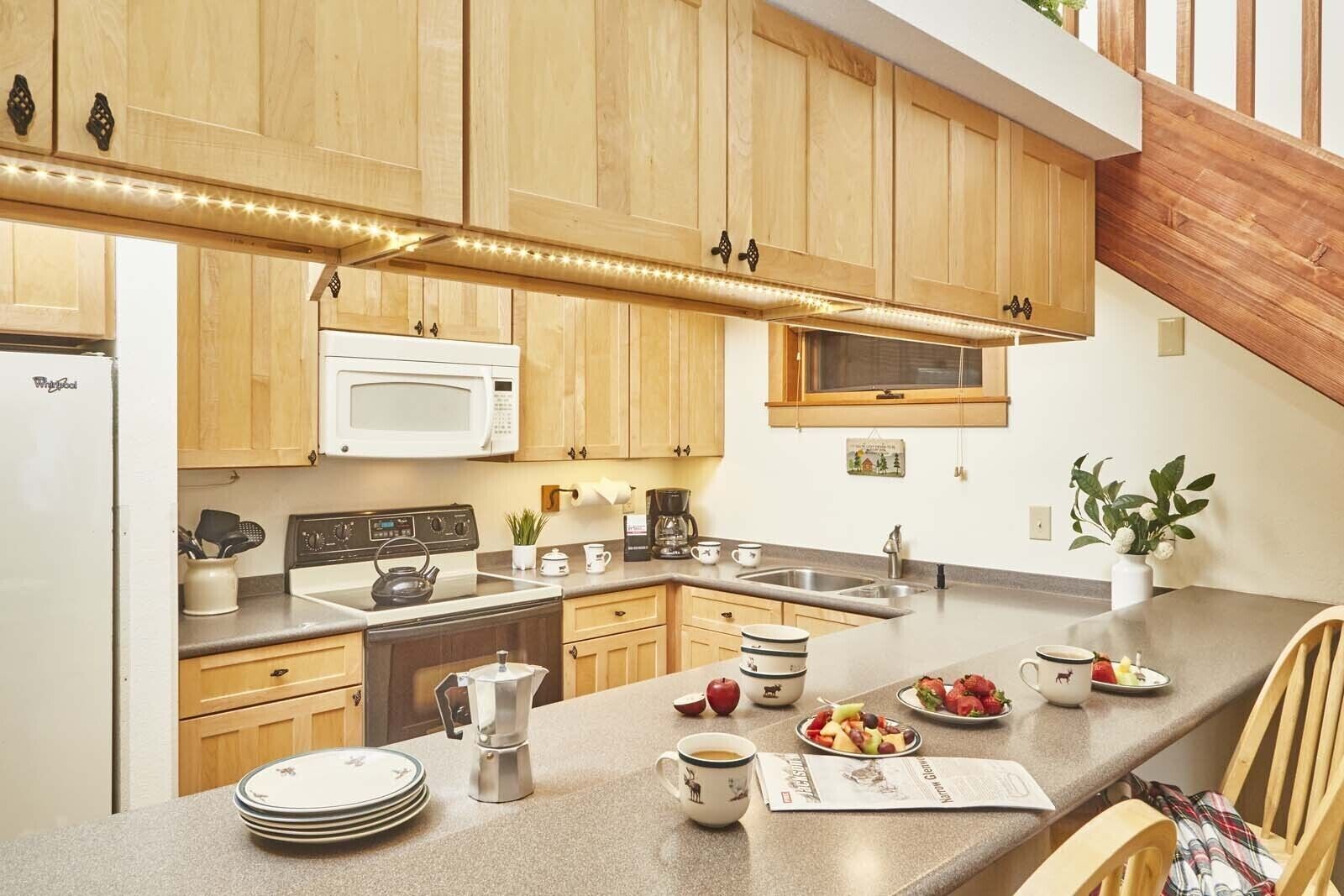 Une cuisine moderne avec des meubles en bois, un four à micro-ondes, une cuisinière et une machine à café. On y trouve un évier et une fenêtre au-dessus du plan de travail.