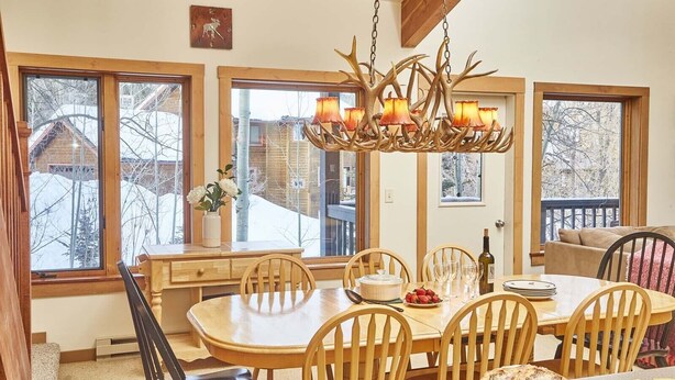 A dining area with a wooden table, chairs, and a chandelier with antler decorations. - JHRL - Rendezvous D4, Great location for families (Teton Village)