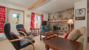 A cozy living room with a stone fireplace, comfortable seating, and a television.