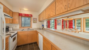 A kitchen with wooden cabinets, a stove, a dishwasher, and a window with red curtains.