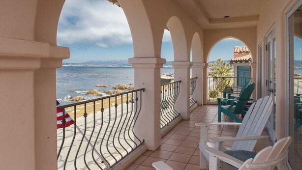 A balcony with a view of the sea, white chairs, and a flag.