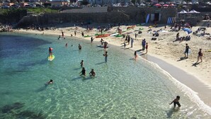 A beach with clear water, people swimming and paddleboarding, and boats on the shore.