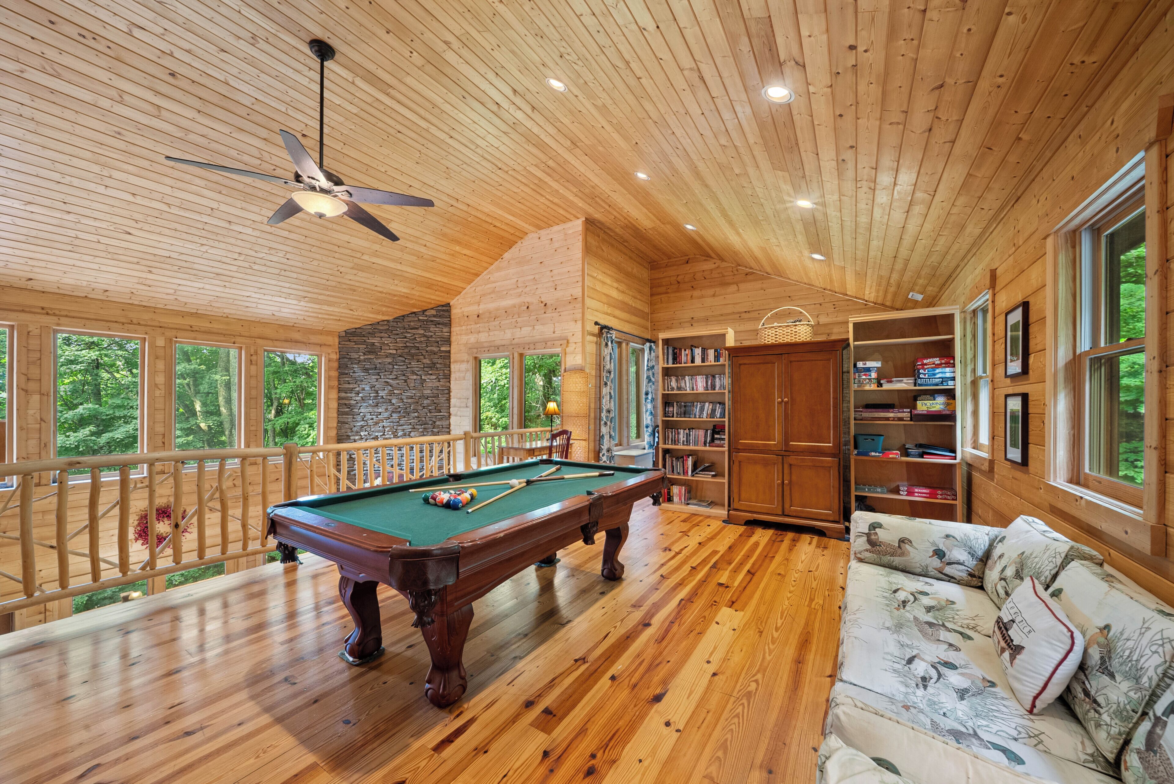 Un interior de madera con una mesa de billar, estanterías y un sofá.